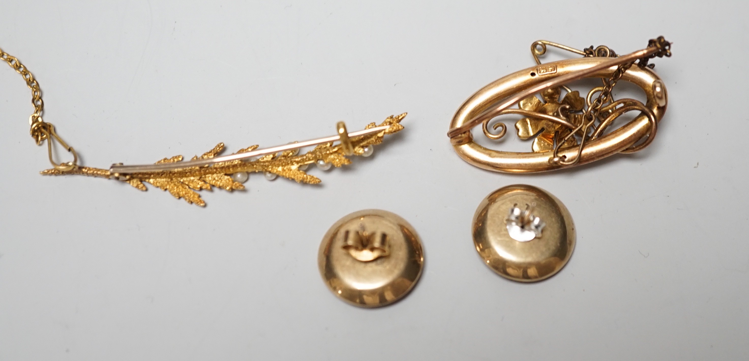 An early 20th century 15ct and seed pearl set leaf brooch, 51mm, one other 15ct and seed pearl brooch and a pair of 15ct, enamelled and gem set ear studs (converted buttons), gross weight 10 grams.